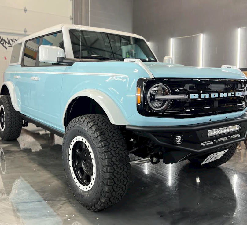 A light blue ford bronco is parked in a garage.