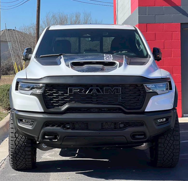 A white ram truck is parked in front of a red building