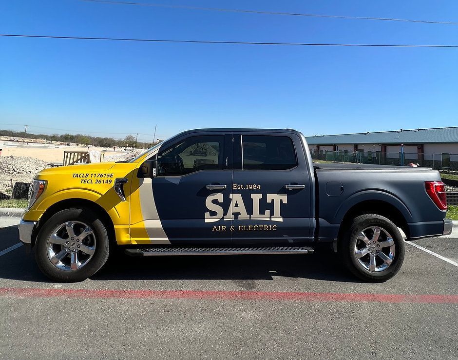 A black and yellow salt truck is parked in a parking lot.