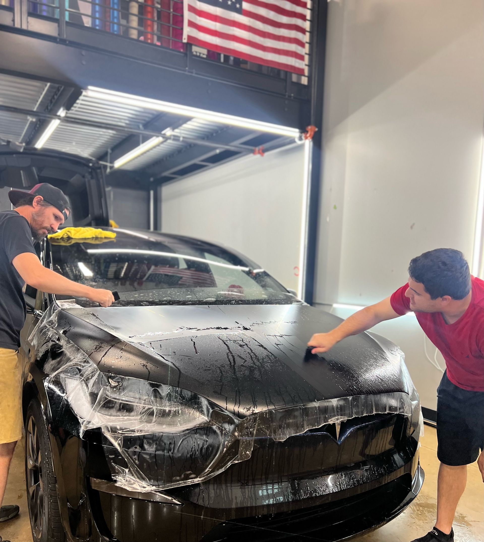 Two men are working on a black car in a garage.