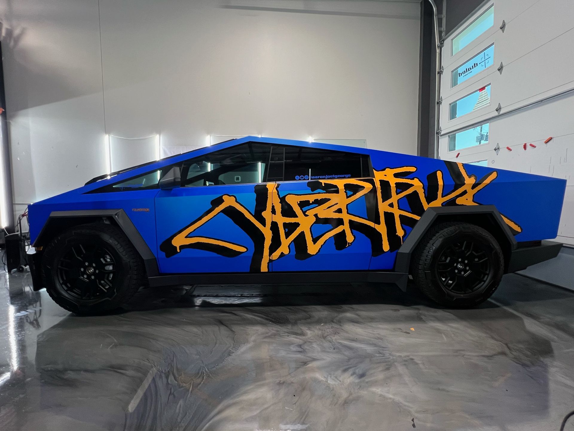 A blue car with graffiti on the side is parked in a garage.