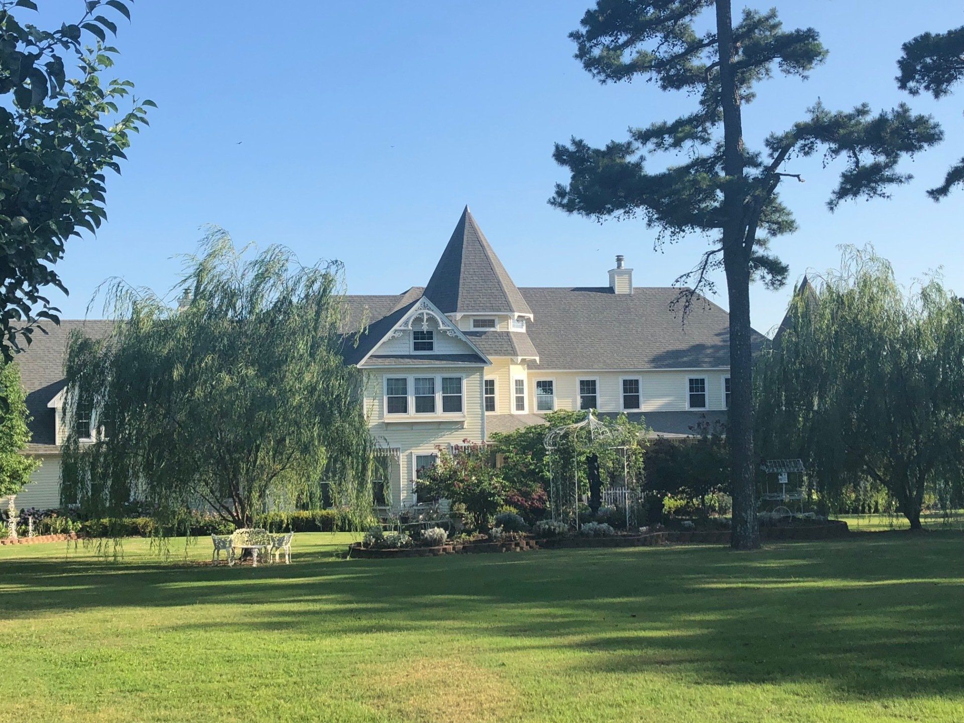 Large white house with a turret, trees, and a green lawn under a clear blue sky.