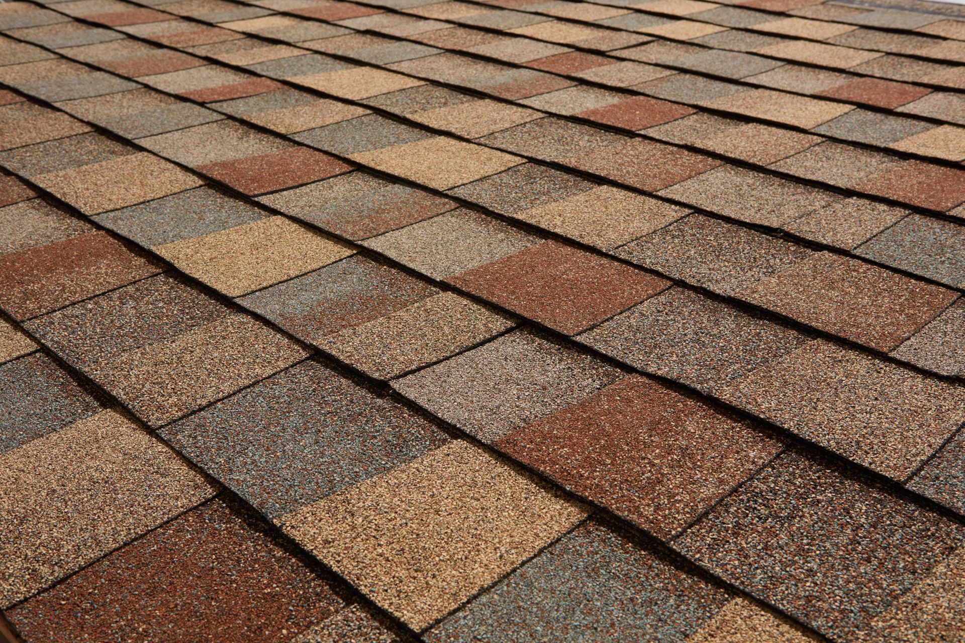 Close-up of asphalt roof shingles in shades of brown, gray, and beige.