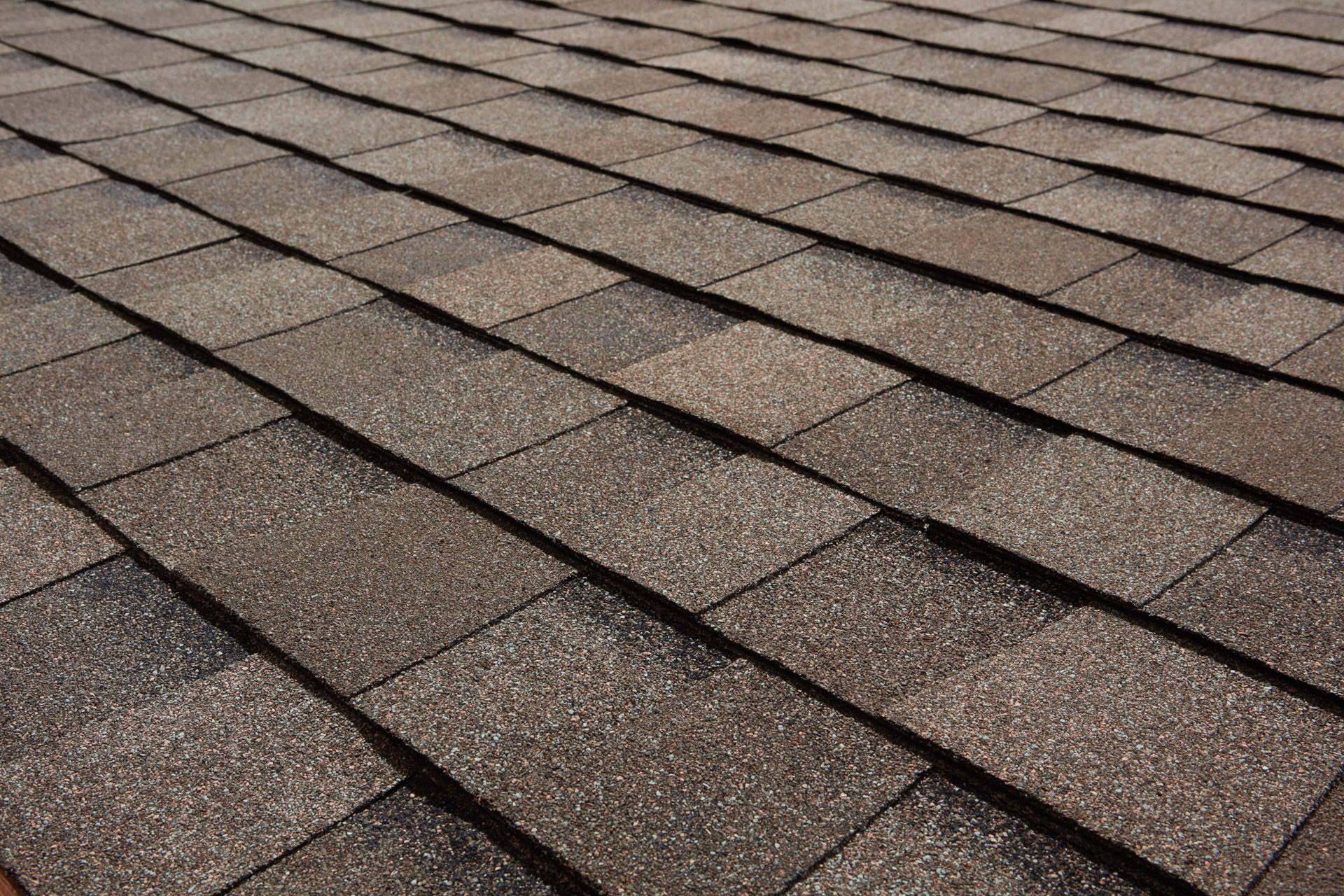 Brown asphalt shingle roof, with a repeating rectangular pattern, viewed at a close angle.