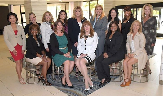 Group of women in business attire posing indoors, smiling.