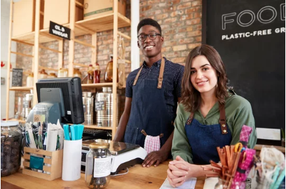 Two smiling shopkeepers behind a counter, in a store with wooden shelves and a sign that reads
