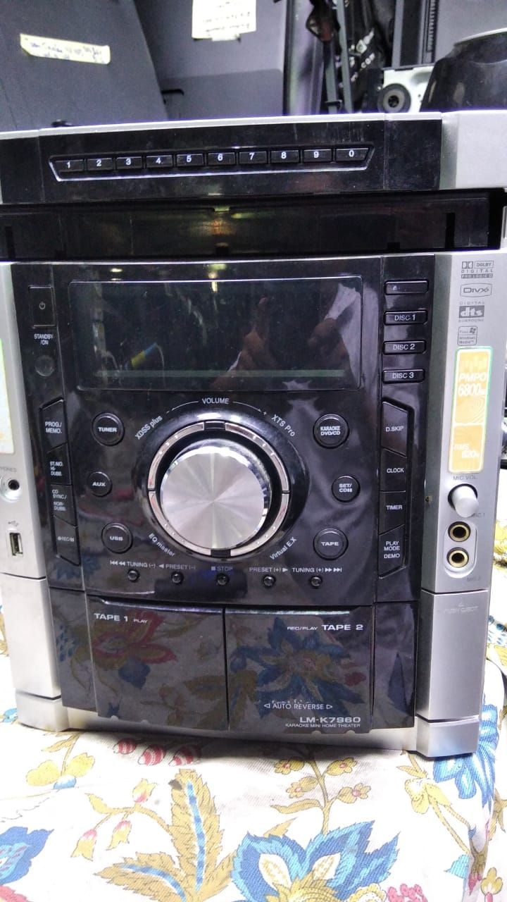Sistema estéreo negro y plateado con un gran dial central, colocado sobre una tela estampada.