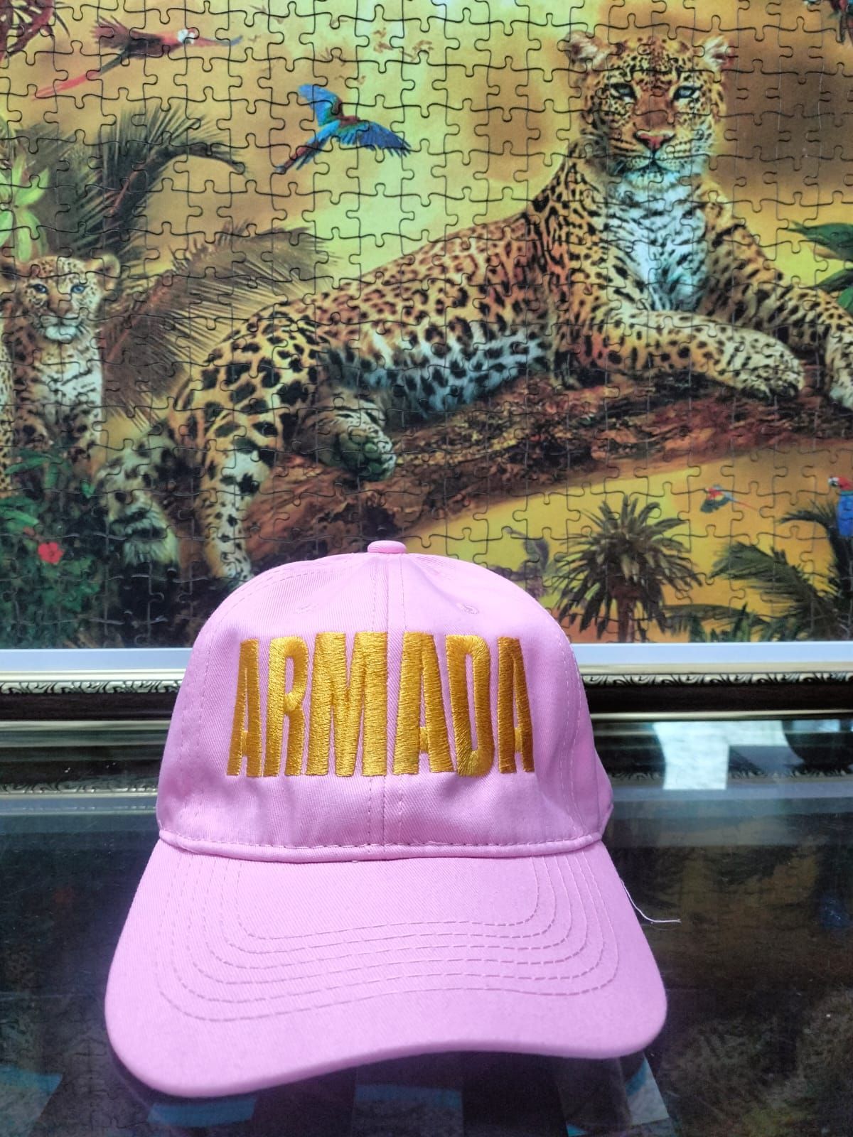 Gorra rosa con el logo de “ARMANI” frente a un mural de leopardo con una mariposa azul y una escena de bosque.