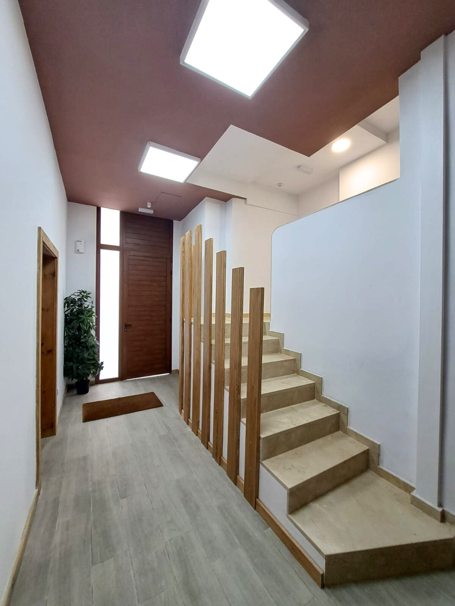 Modern entryway featuring a wooden staircase with vertical slat railing, light wood flooring, and recessed ceiling lights.