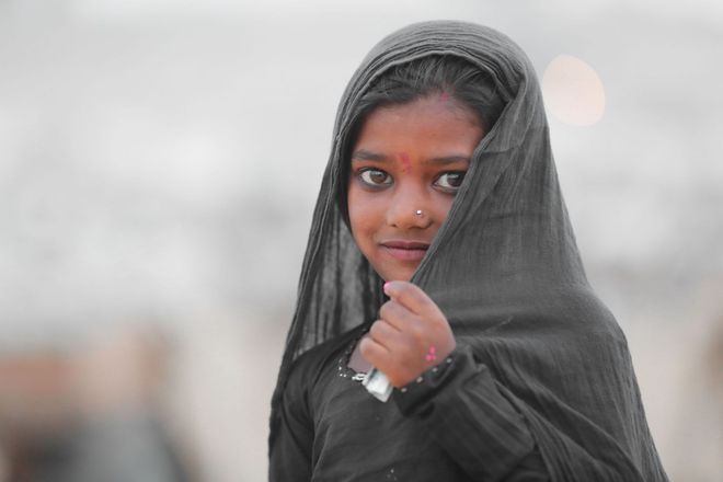 A person in a black veil looks at the camera while holding the fabric near their face.