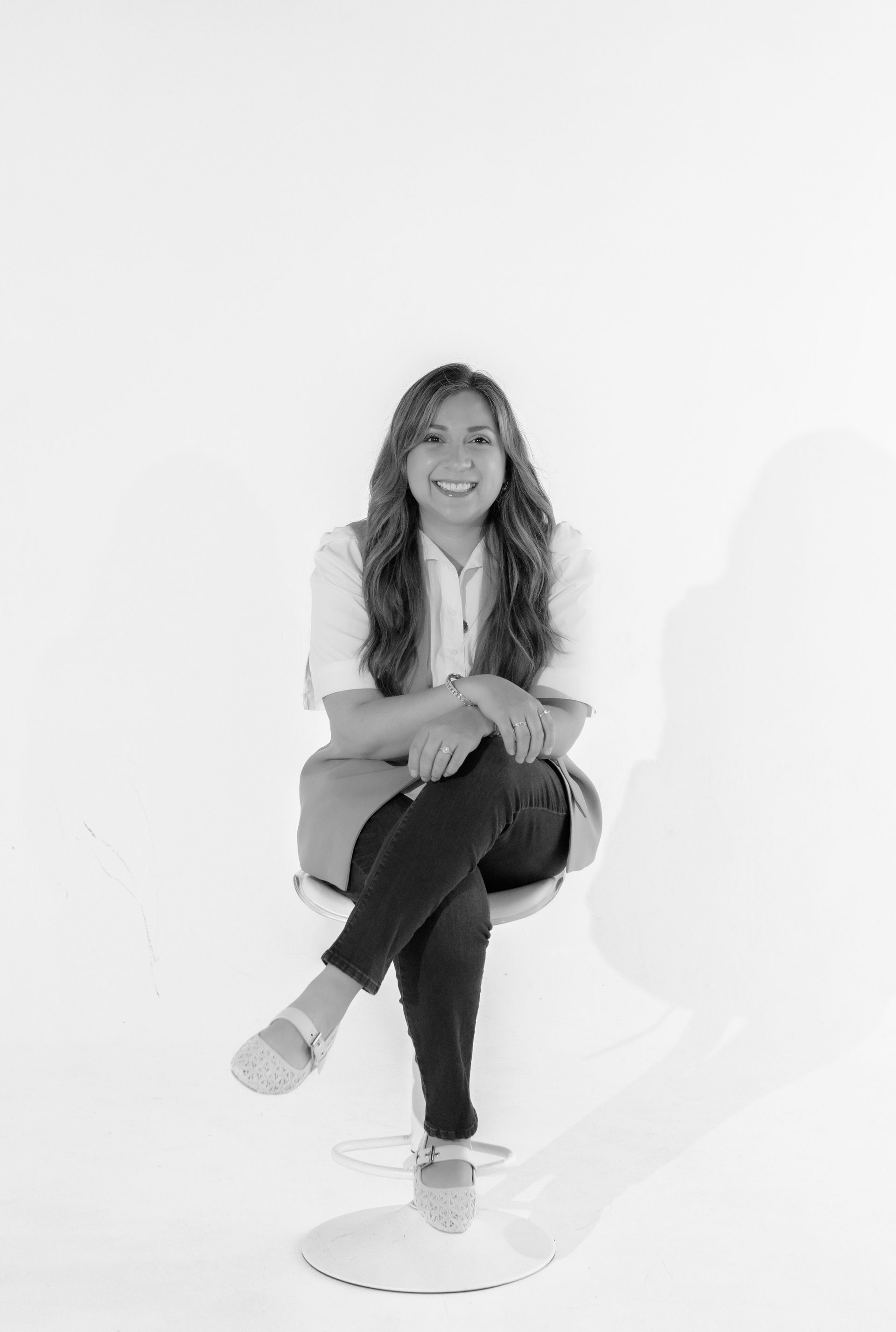 A woman is sitting on a white chair with her legs crossed.