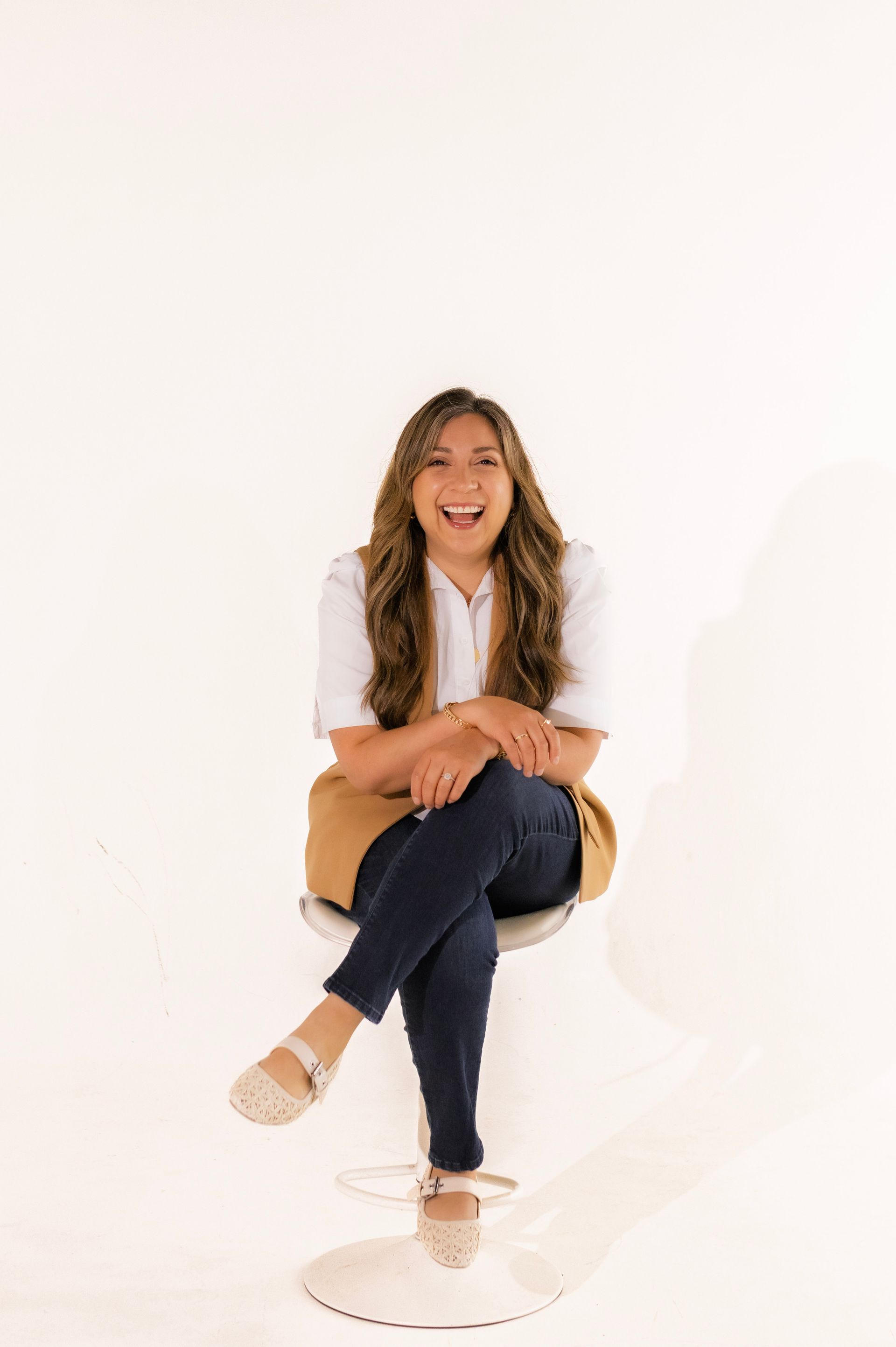 A woman is sitting on a chair with her legs crossed and smiling.