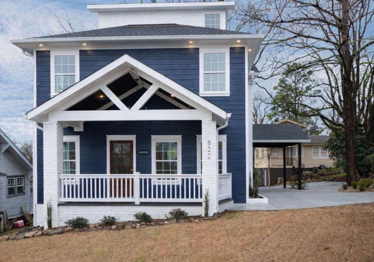 Blue and white two-story house with a porch and carport; brown door, bare trees, and a concrete driveway.