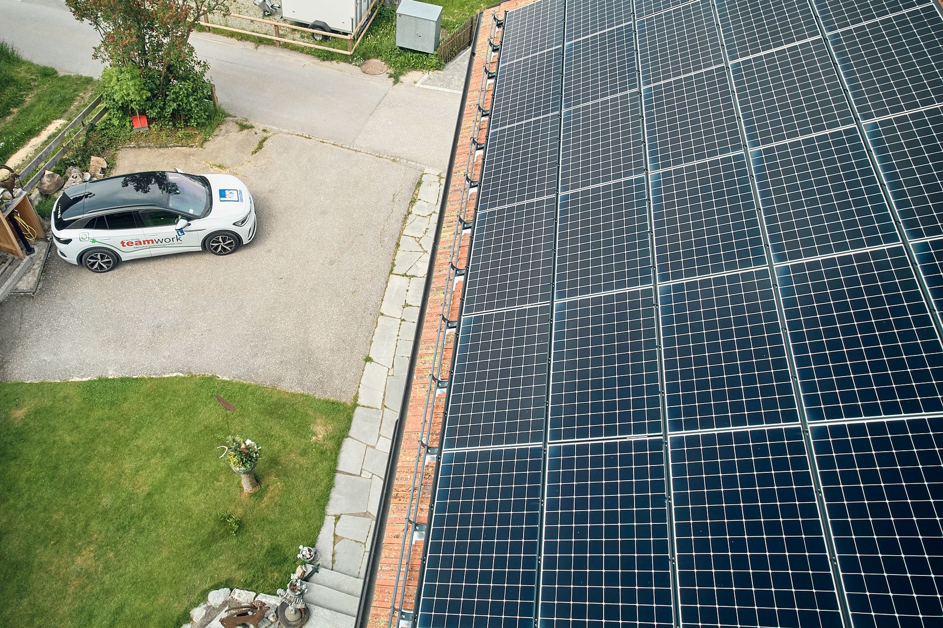 Eine Luftaufnahme eines Hauses mit Solarmodulen auf dem Dach und einem Elektro Auto