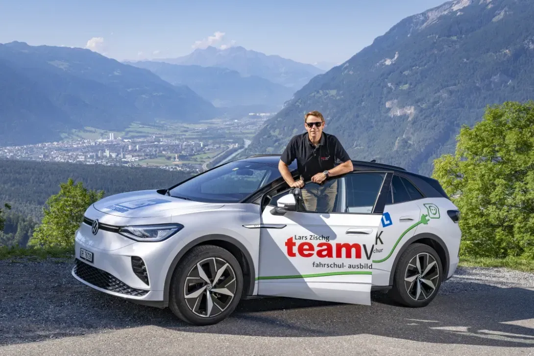 Fahrlehrer Lars Zischg steht neben einem weißen Auto mit dem Wort „Team“ auf der Seite.
