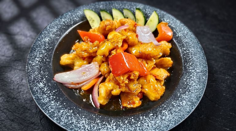 Orange-glazed fried chicken on a black plate with red onion slices and cucumber wedges