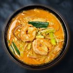Bowl of orange shrimp noodle soup with green vegetables, viewed from above