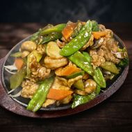 Plate of stir-fried vegetables and meat with green snow peas, carrots, and mushrooms on a dark table