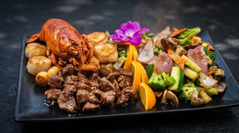 Grilled meat, chicken, and vegetables arranged on a black platter, garnished with a purple flower