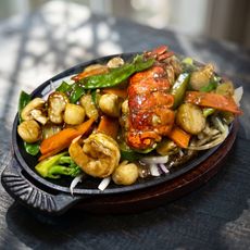 Sizzling mixed seafood and vegetables on a cast-iron platter with a lobster tail