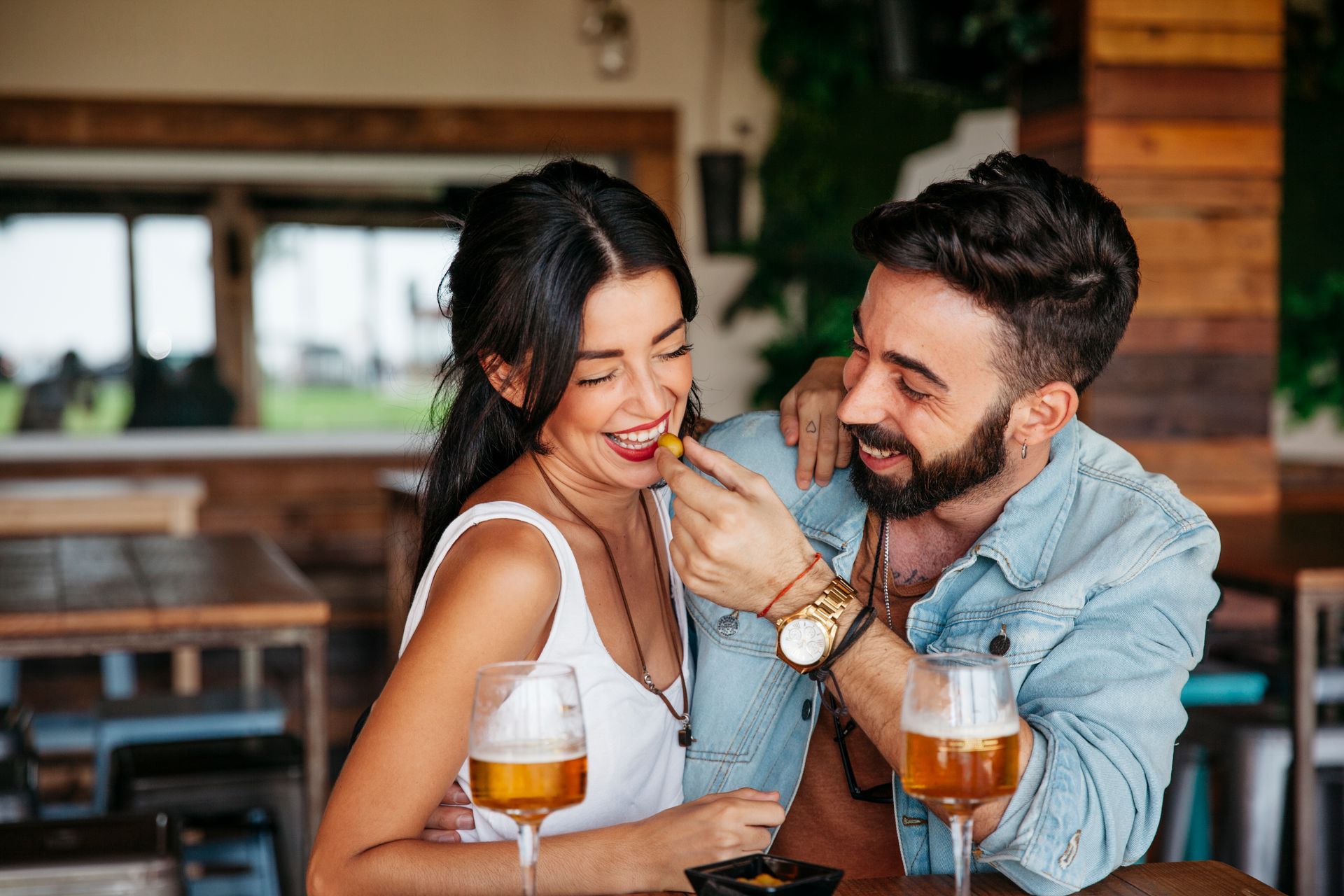 Couple smiling at a café table, clinking drinks and chatting by the window.