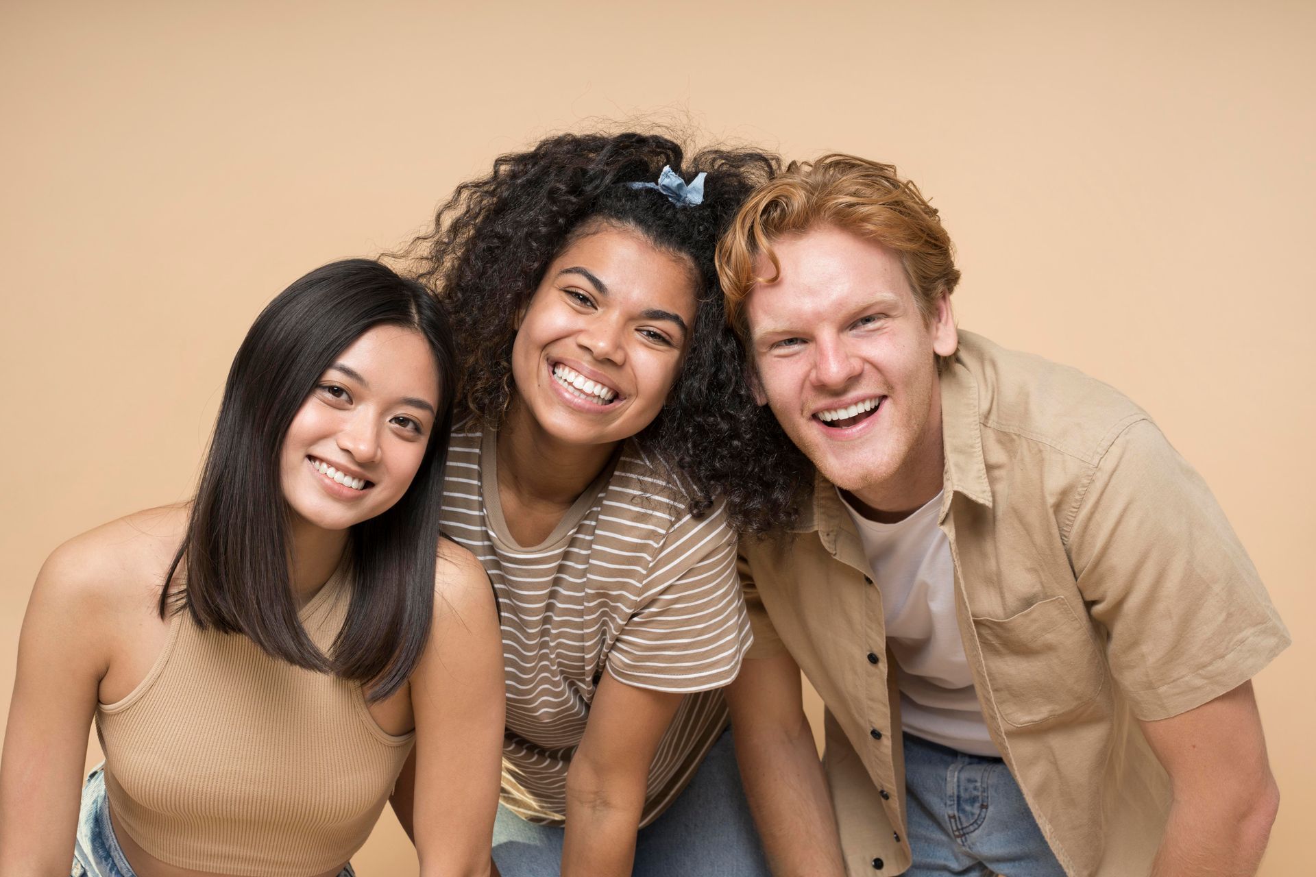 Three diverse young adults smiling and laughing against a neutral background.