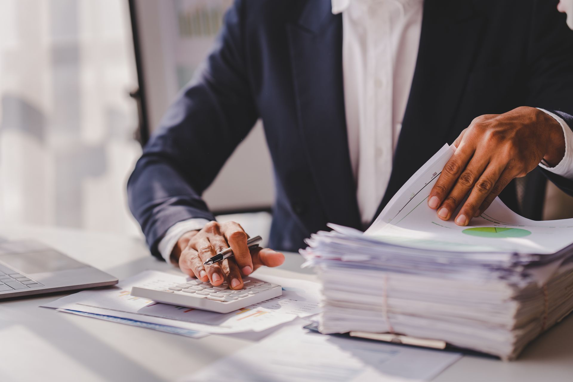 Businessperson sorting documents at a desk with a calculator and a large stack of papers