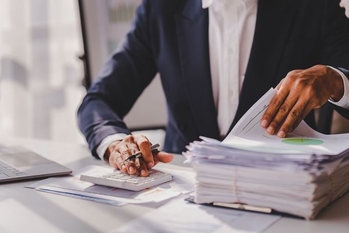 Businessperson sorting documents at a desk with a calculator and a large stack of papers