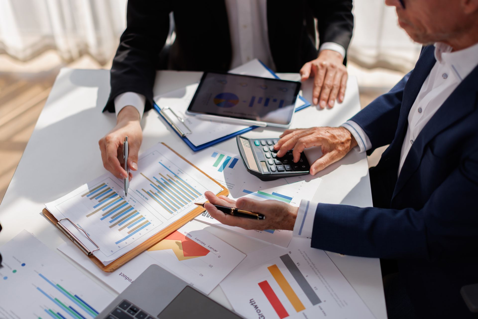 Business meeting with two people reviewing charts and financial reports at a desk, with a laptop and tablet