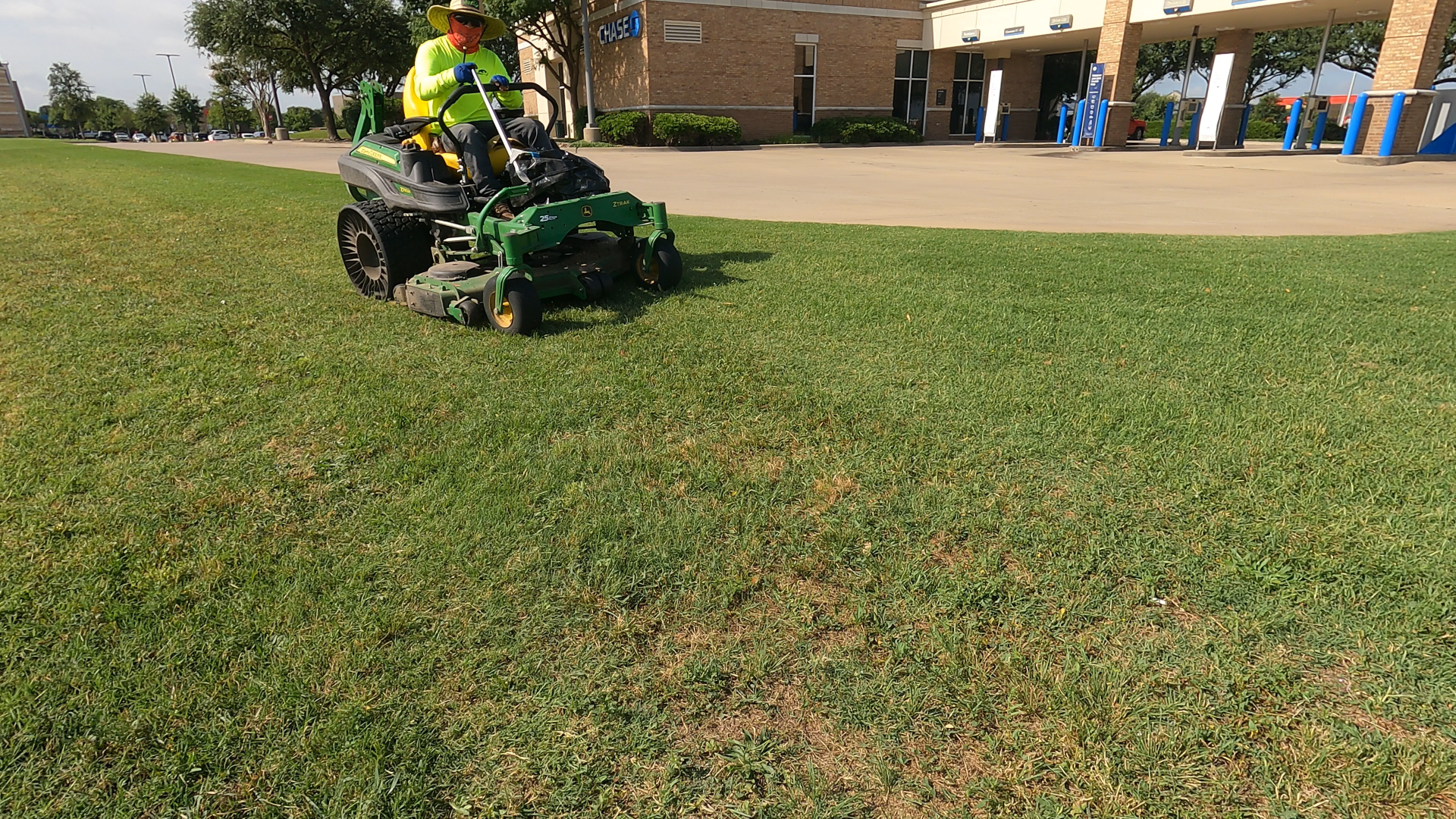 A person mowing a lawn with a riding mower in a park near a building.