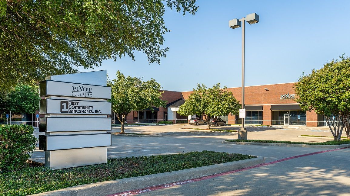Office building exterior with sign, driveway, trees, and a bright blue sky.