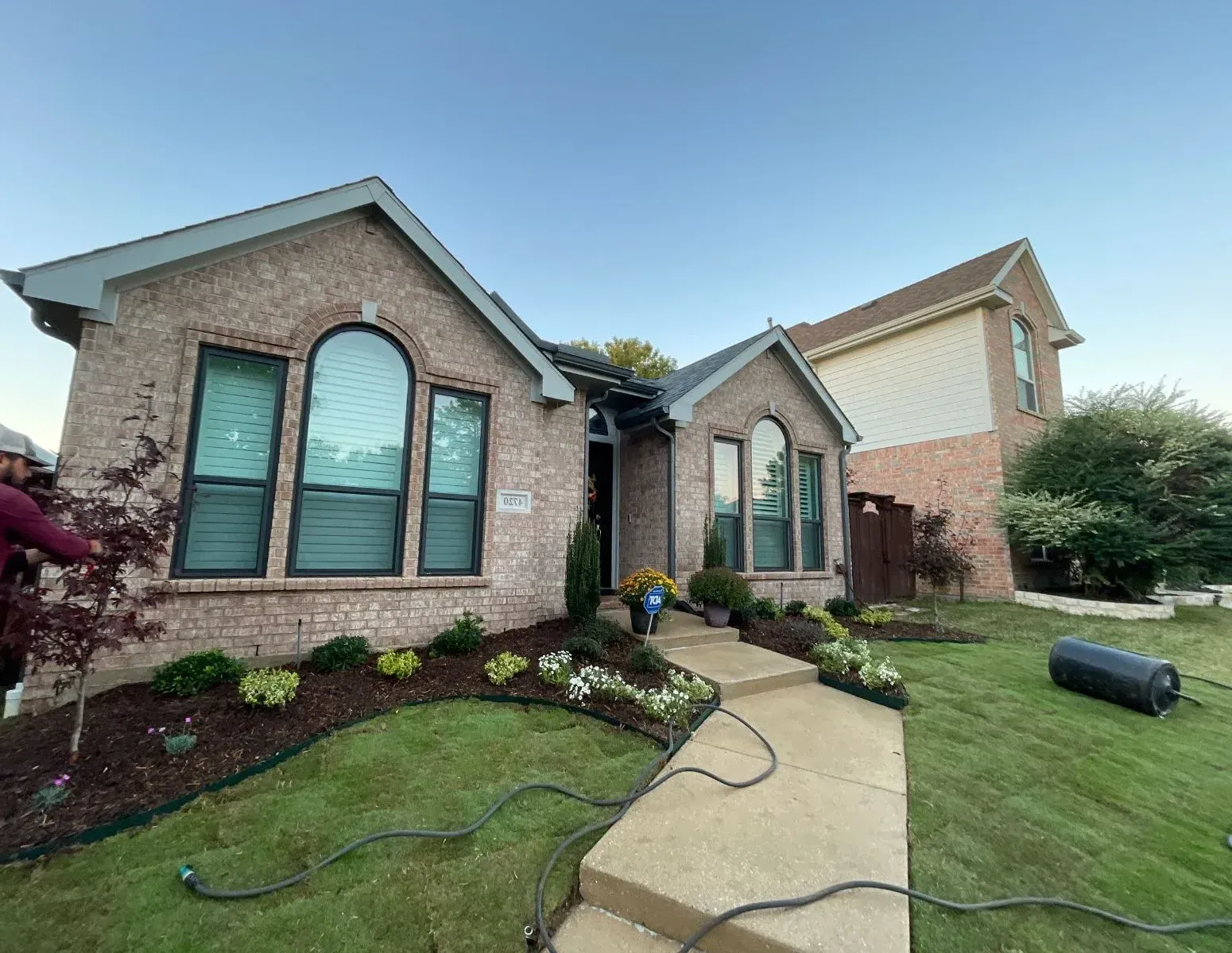 Brick house with manicured landscaping and a concrete walkway leading to the front door.