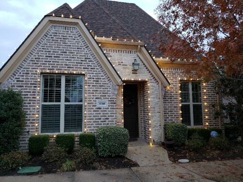 House with warm white Christmas lights on brick exterior.