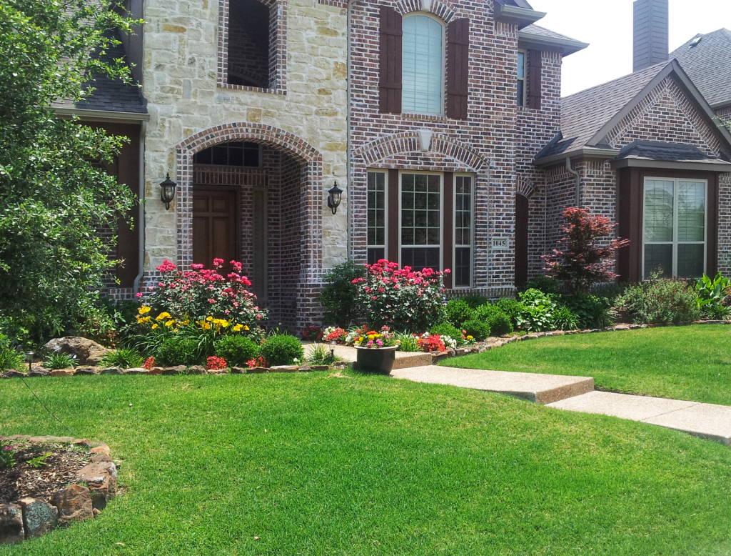Stone and brick house with colorful flower beds and green lawn.