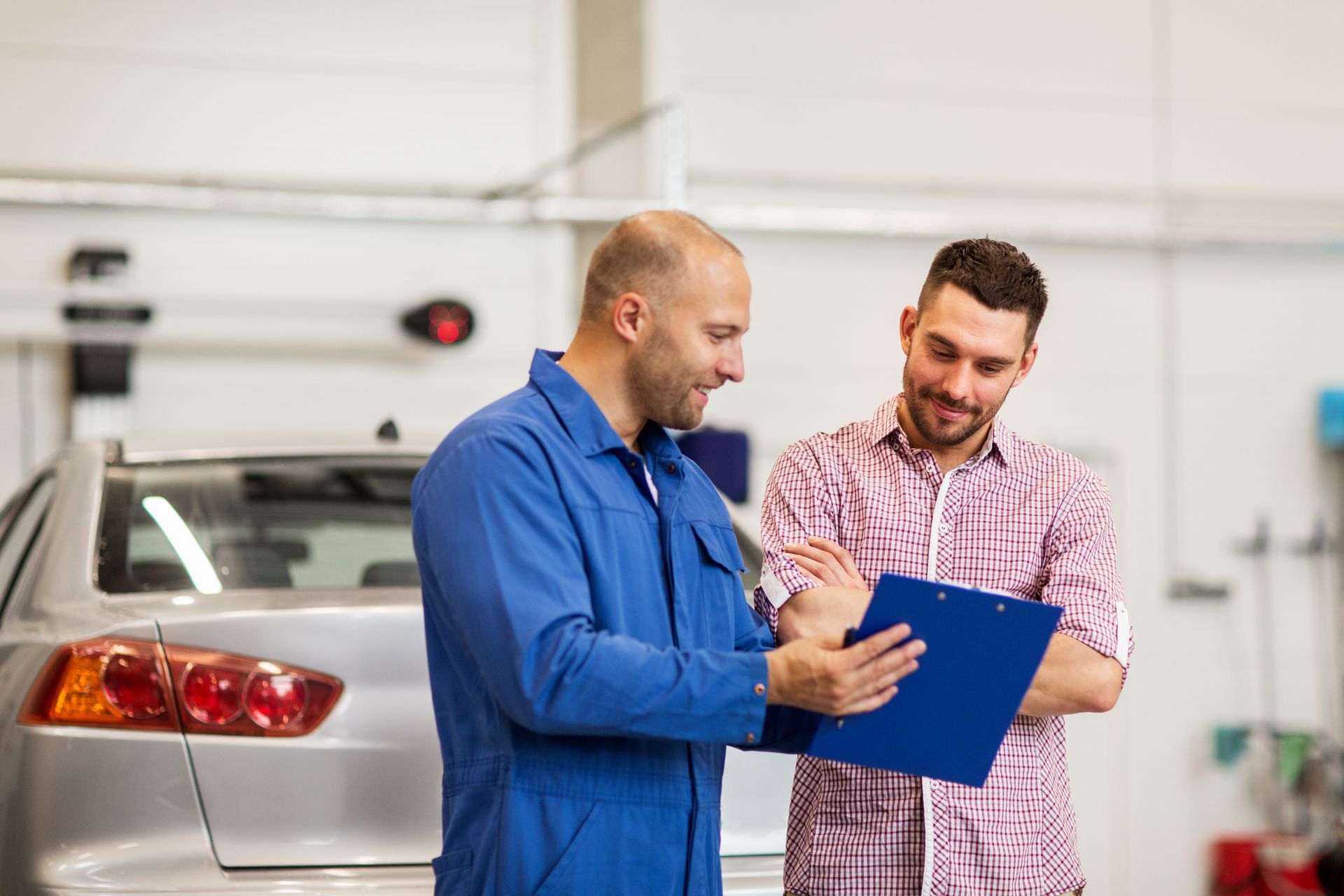 Two people in a car workshop reviewing a clipboard beside a parked vehicle.