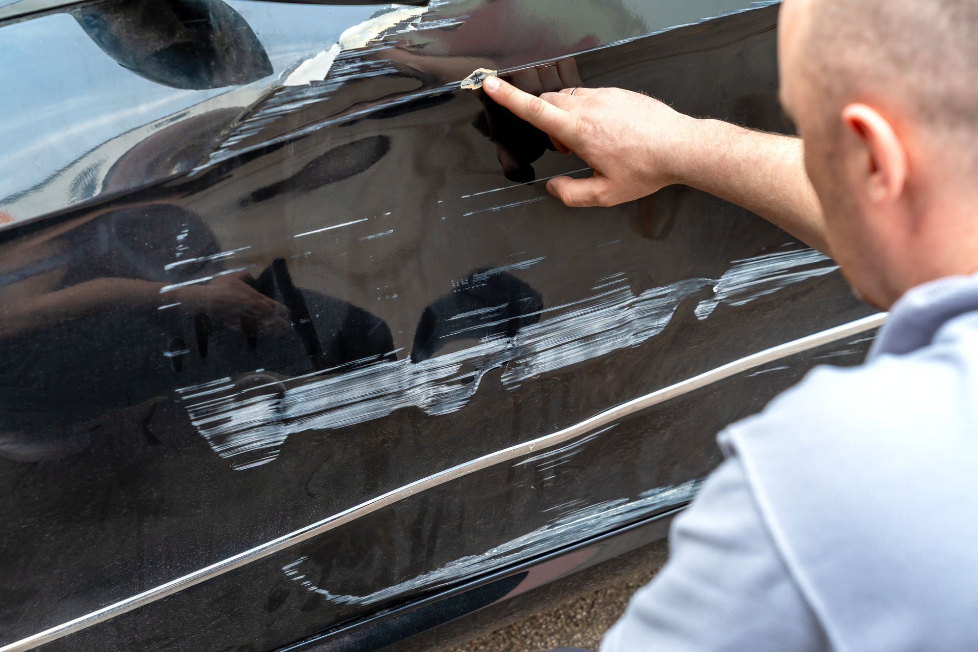 Person inspecting deep scratches and dents on a damaged black car door.