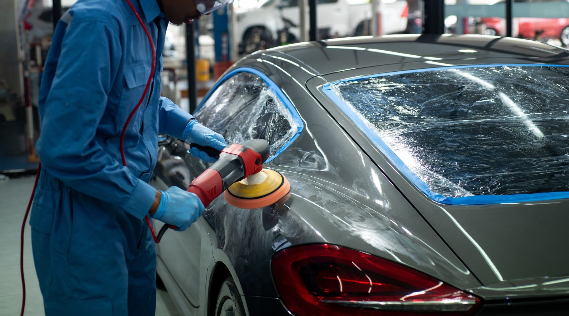An auto body shop technician polishing a car after paint and dent repair.