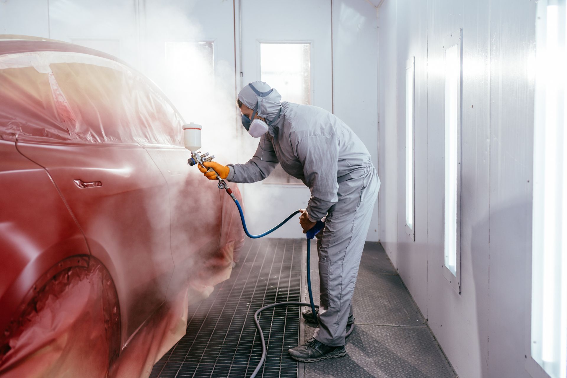 Auto body technician spray-painting a red car inside a paint booth. Auto body technician spray-painting a red car inside a paint booth.