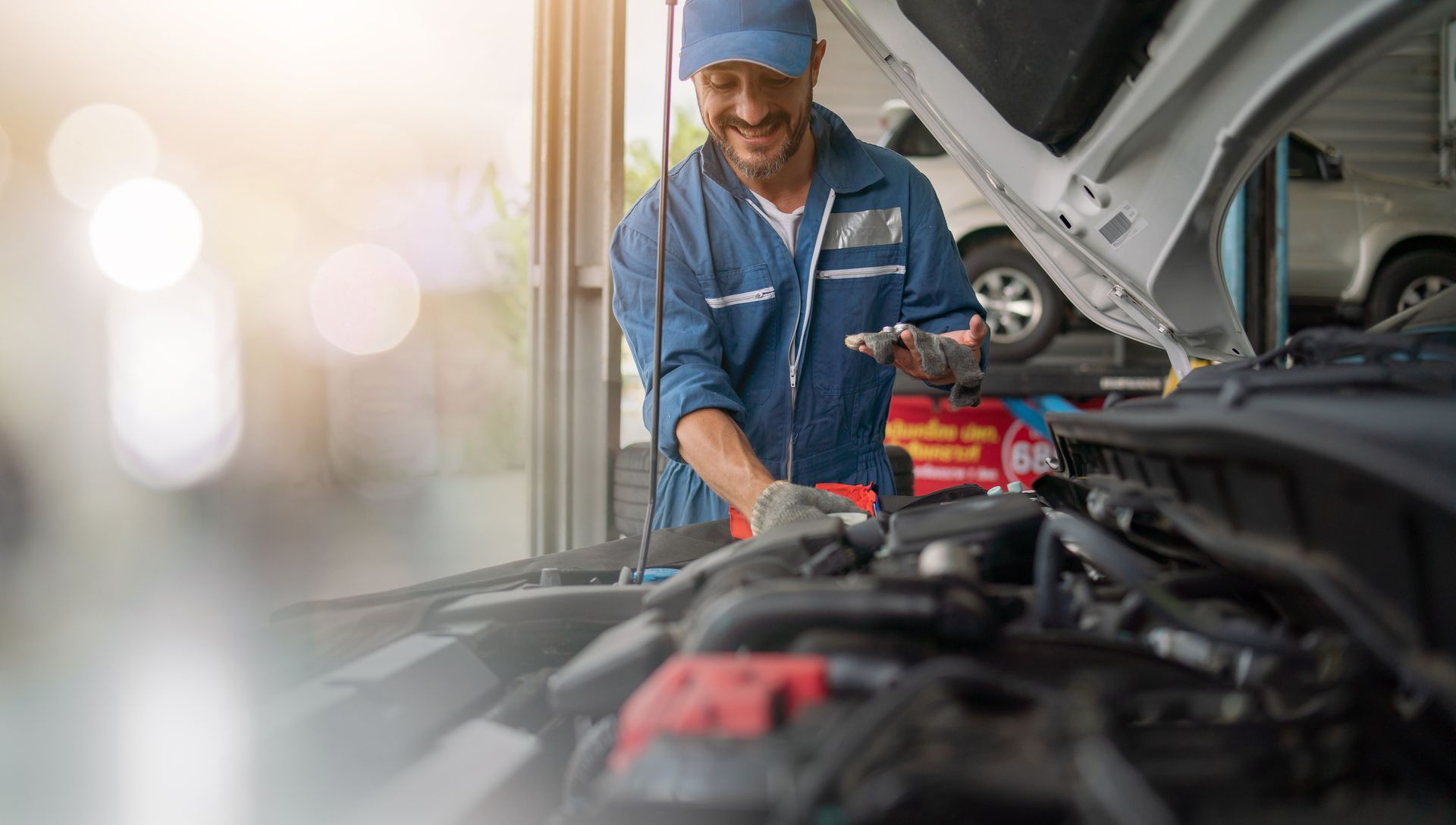Mechanic in blue uniform working on car engine in auto repair shop.
