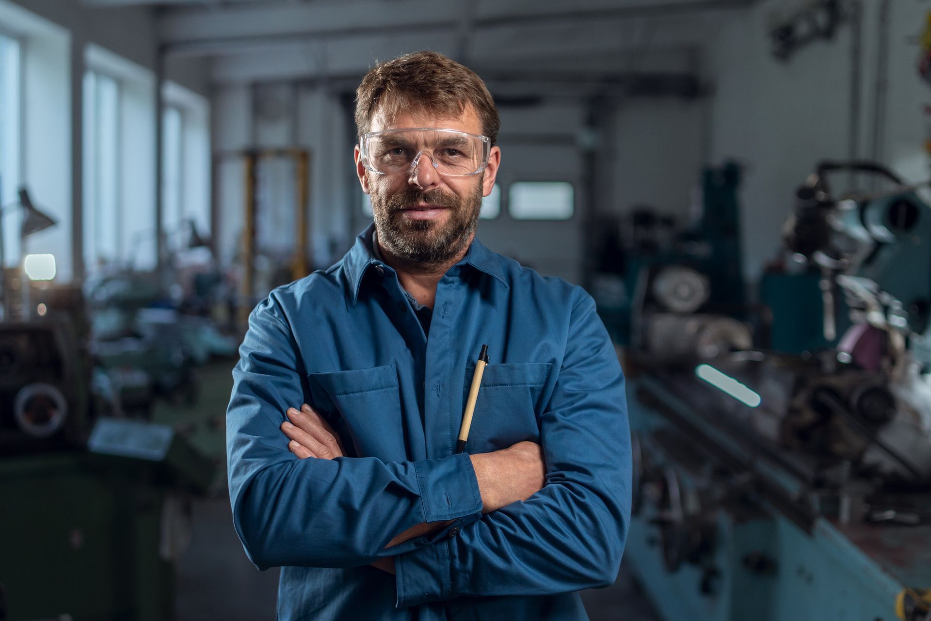 Mechanic in blue uniform standing in auto shop with arms crossed.