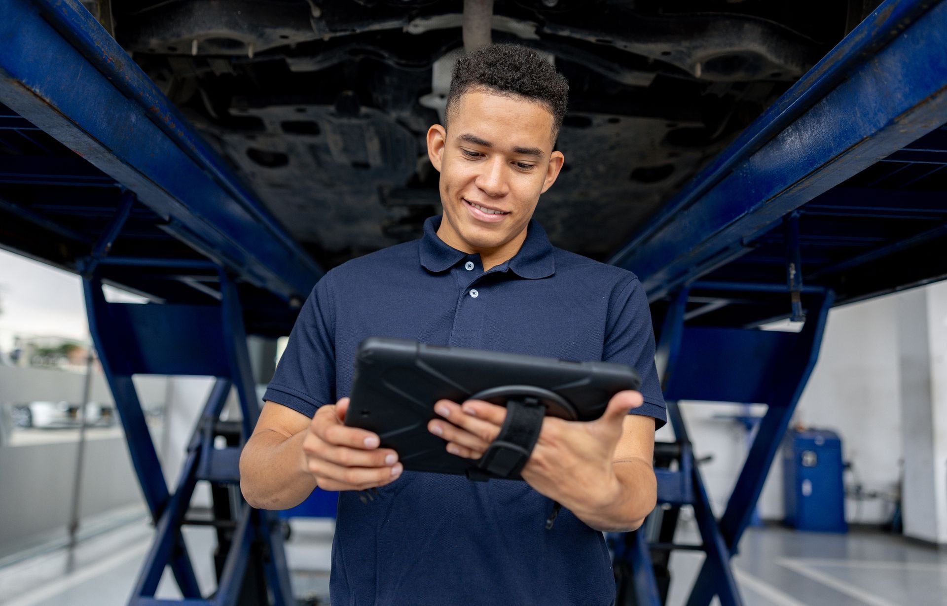 Mechanic using tablet under lifted car in auto repair shop. Mechanic using tablet under lifted car in auto repair shop.