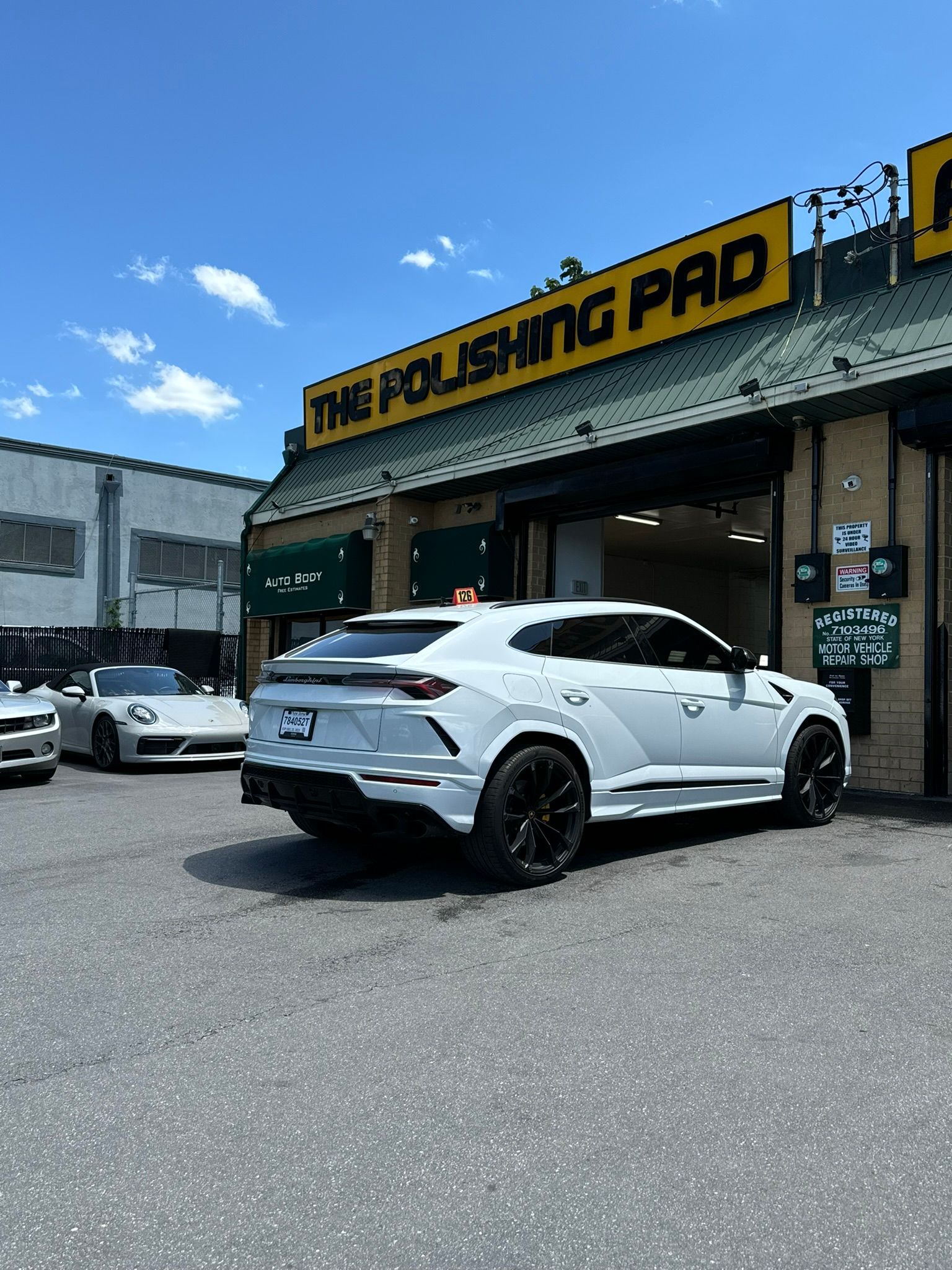 White Lamborghini Urus parked at The Polishing Pad shop on a sunny day.
