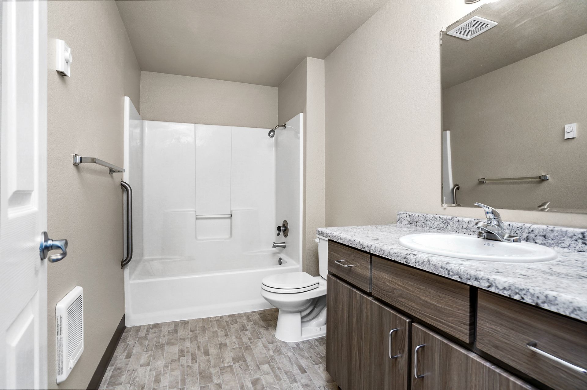 Modern bathroom with a bathtub-shower combo, toilet, and granite vanity with a sink, mirror, and wood-toned cabinets.