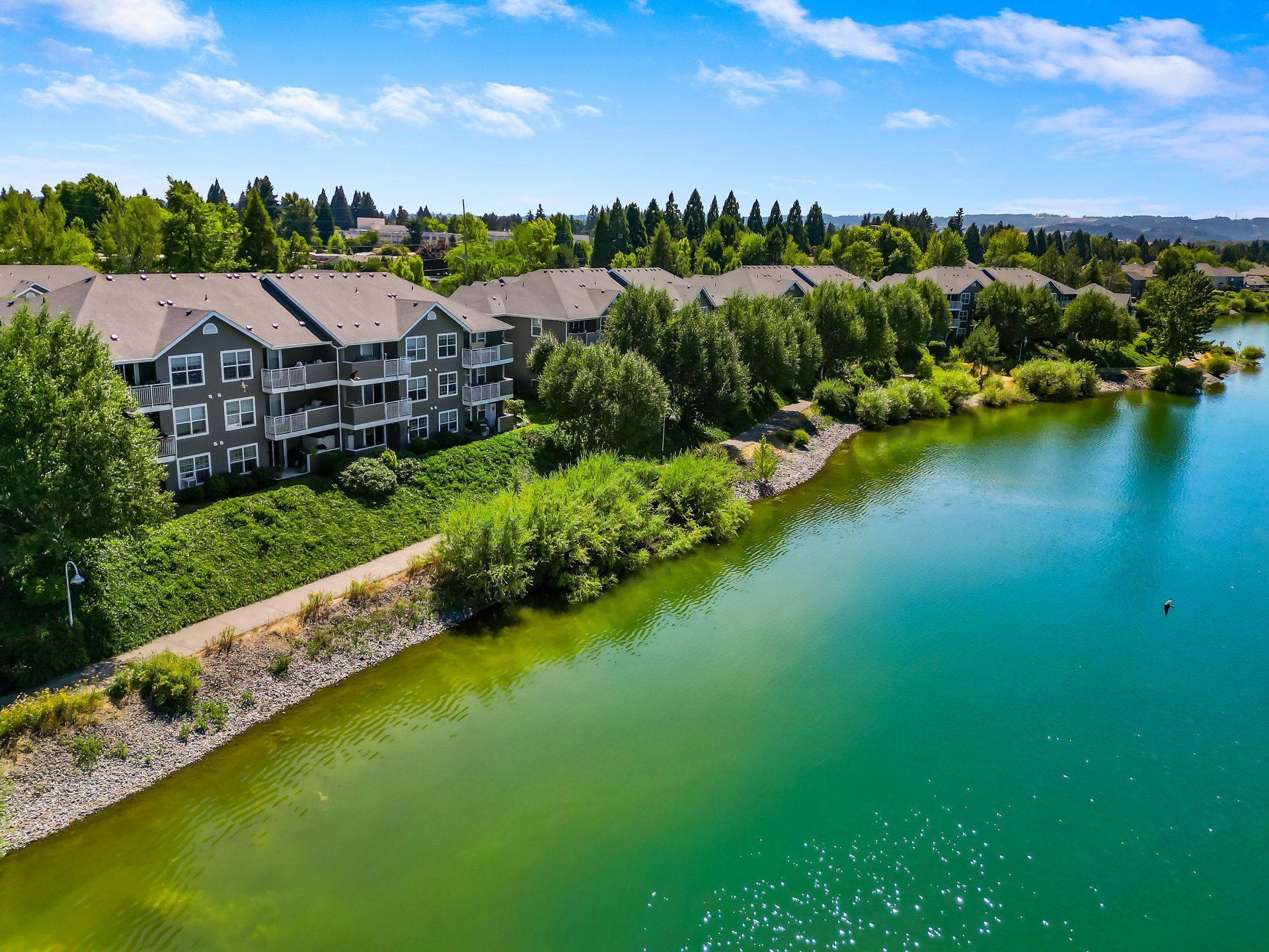 Aerial view of a multi-story apartment complex along the shore of a vibrant turquoise lake surrounded by trees.