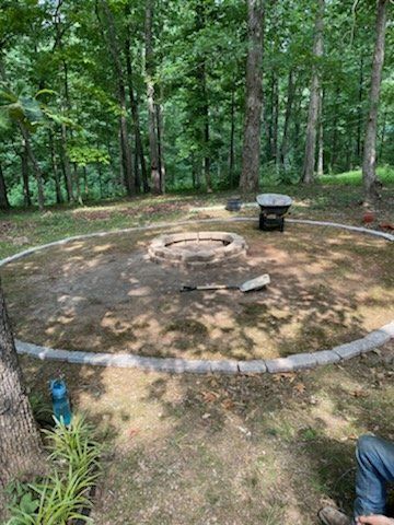 Backyard fire pit area with a stone ring, seating, and trees surrounding the clearing