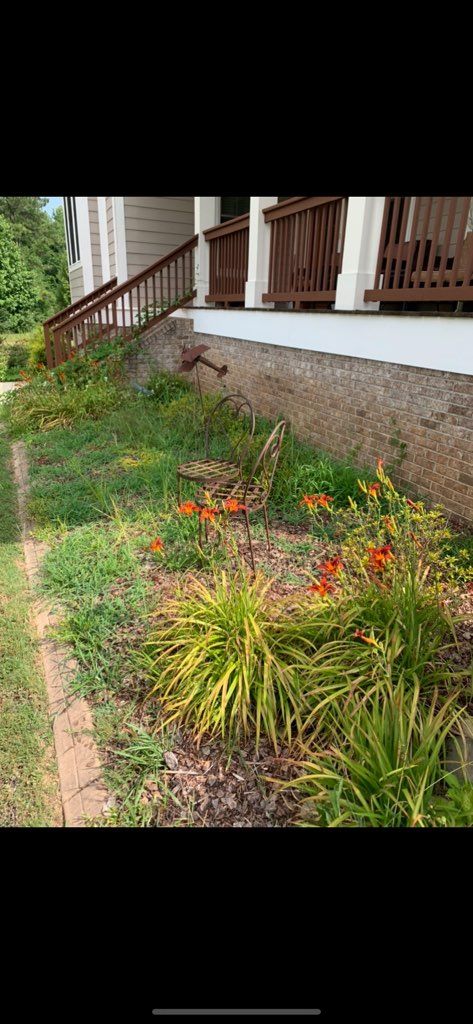 Garden bed with orange flowers and green plants beside a house porch and stone foundation