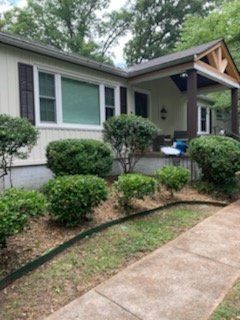 Single-story house with a front porch, trimmed shrubs, and a concrete walkway