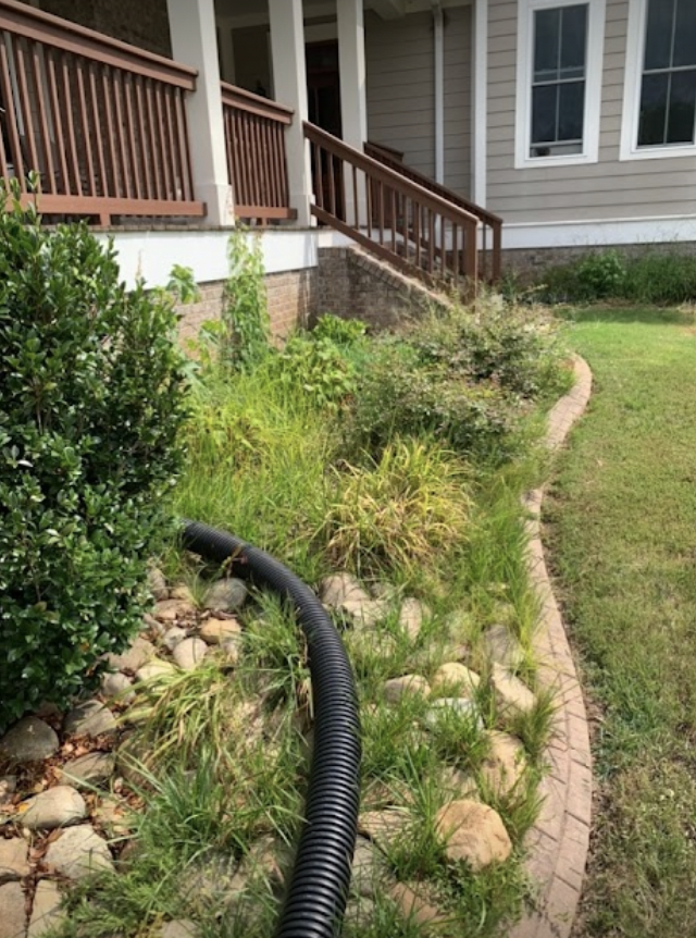 Front yard with a black hose, stone edging, and a porch beside a house.