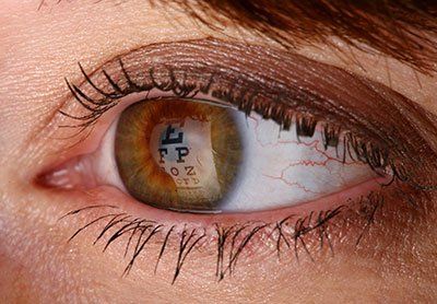 Close-up of an eye reflecting a Snellen eye chart; brown iris with visible blood vessels.
