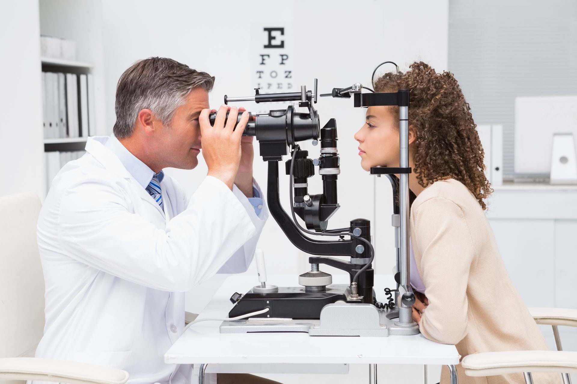 Eye doctor performing a vision exam using a slit lamp in a clean optometry office.